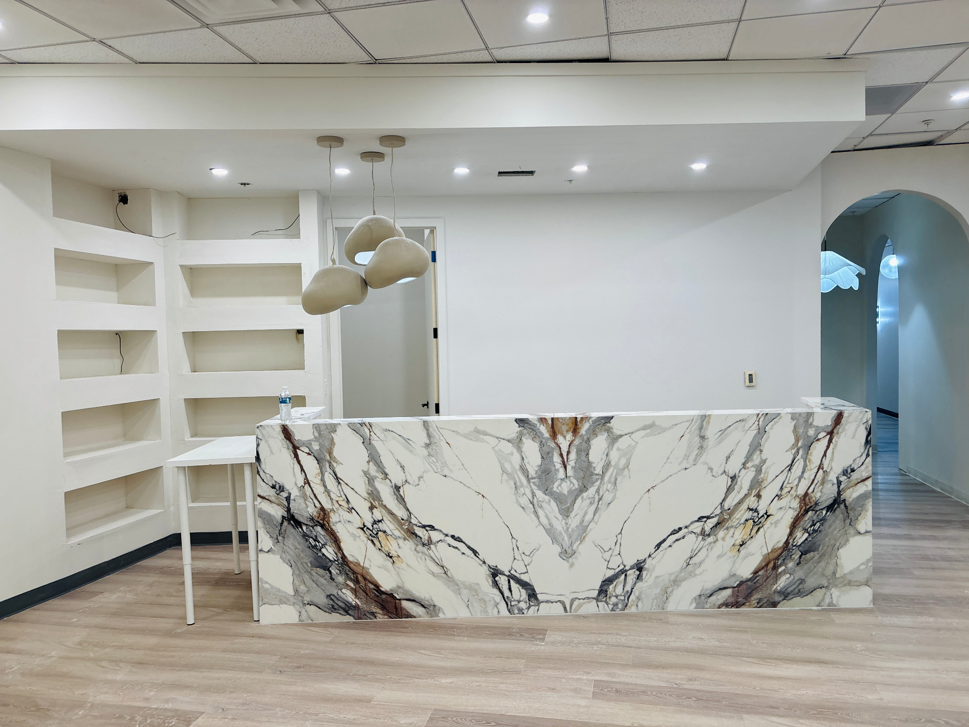 Office reception with a marble-wrapped desk, bare walls and empty niche shelving before the remodel
