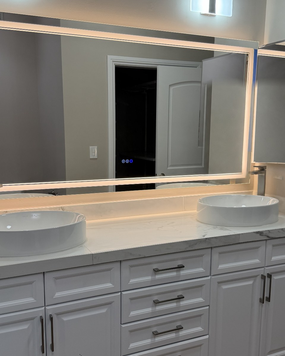 Double vanity with two vessel sinks, a marble-look countertop and a large backlit LED mirror