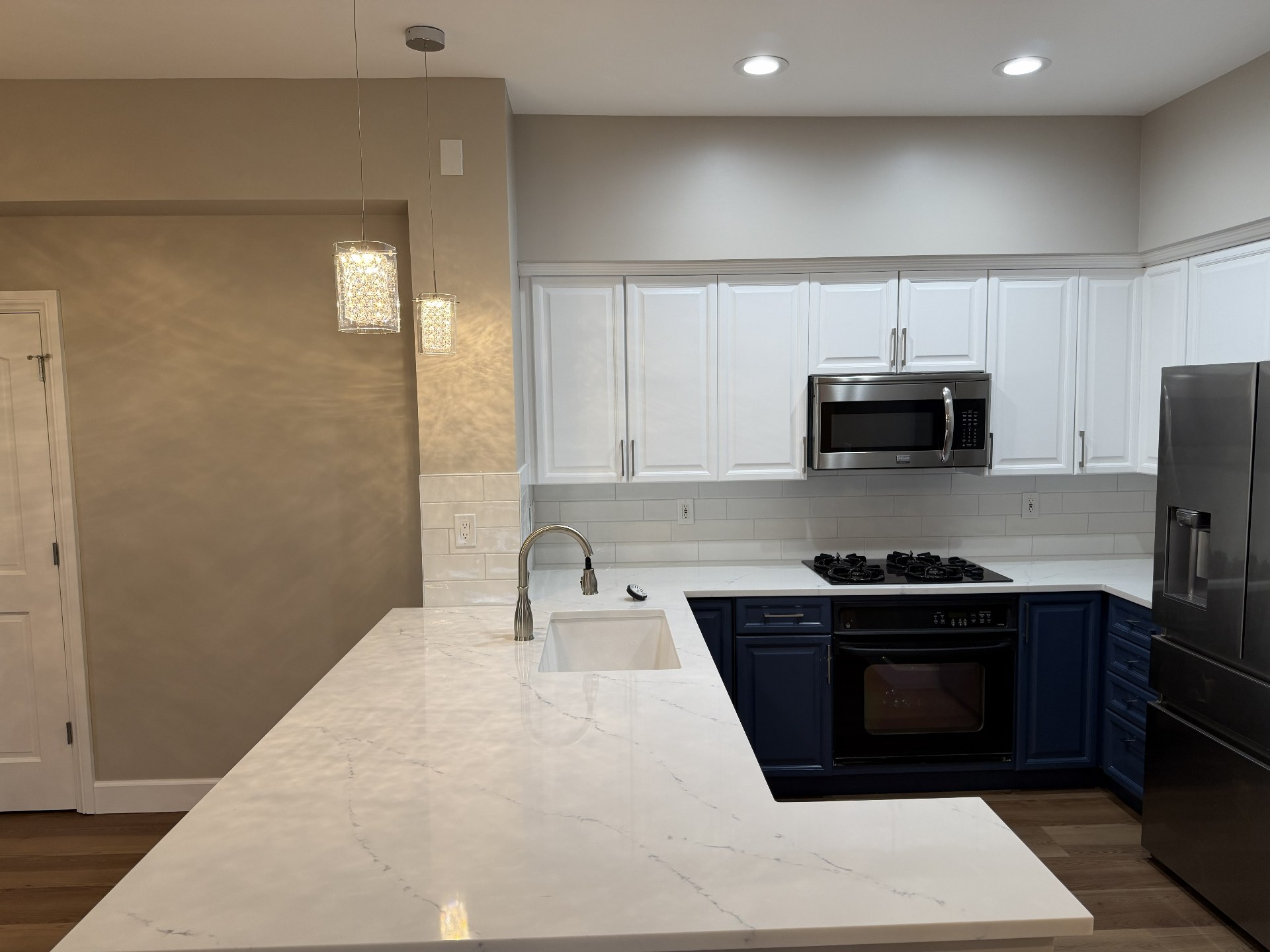 Finished kitchen with white upper cabinets, navy lower cabinets, white quartz countertops and pendant lighting