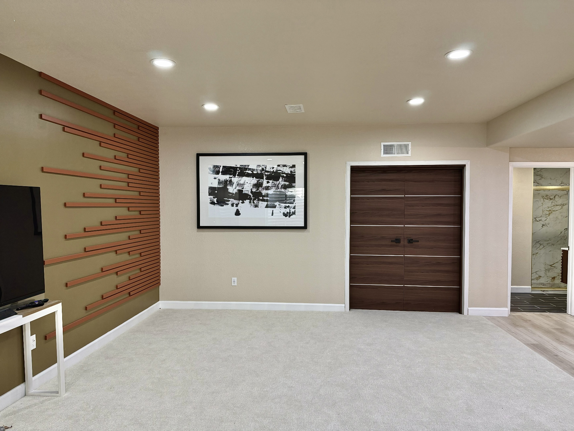 Finished family room with a terracotta slat accent wall, framed artwork, double wood doors and cream carpet