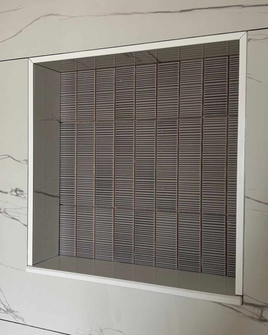 Close-up of a tiled shower niche with grey ribbed tile set into a marble-look wall