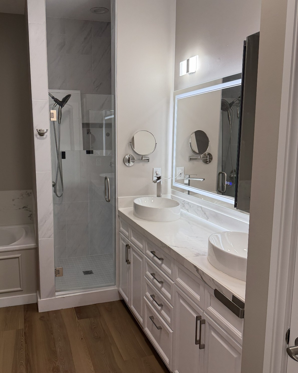 Bathroom with a soaking tub, glass walk-in shower, double vanity and wood-look plank flooring