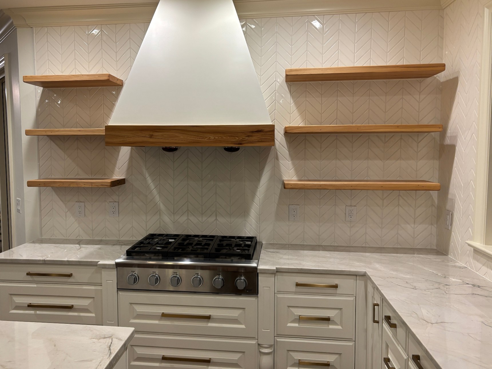 Cooking area with a white range hood, herringbone tile backsplash, wooden floating shelves and a professional-style range