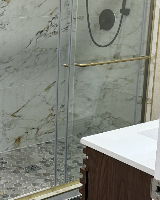 Walk-in shower with black floor tile, brass-framed glass doors and a marble-look surround