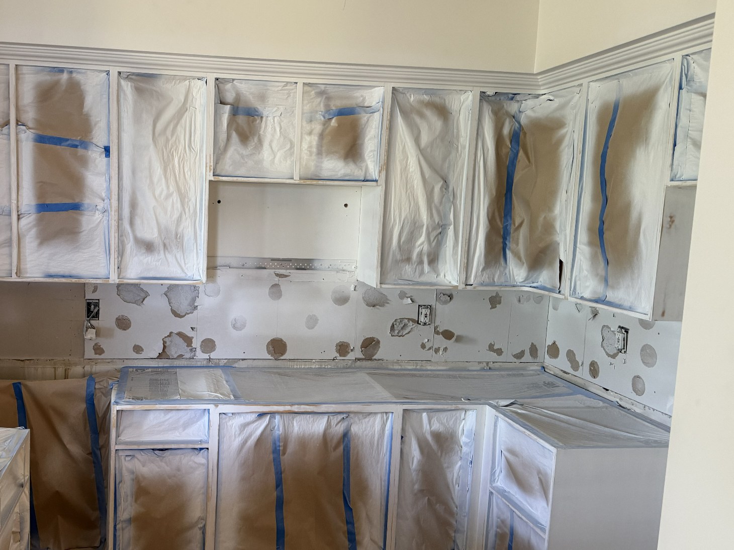 Kitchen mid-renovation with cabinets masked in protective paper and walls prepared for the backsplash