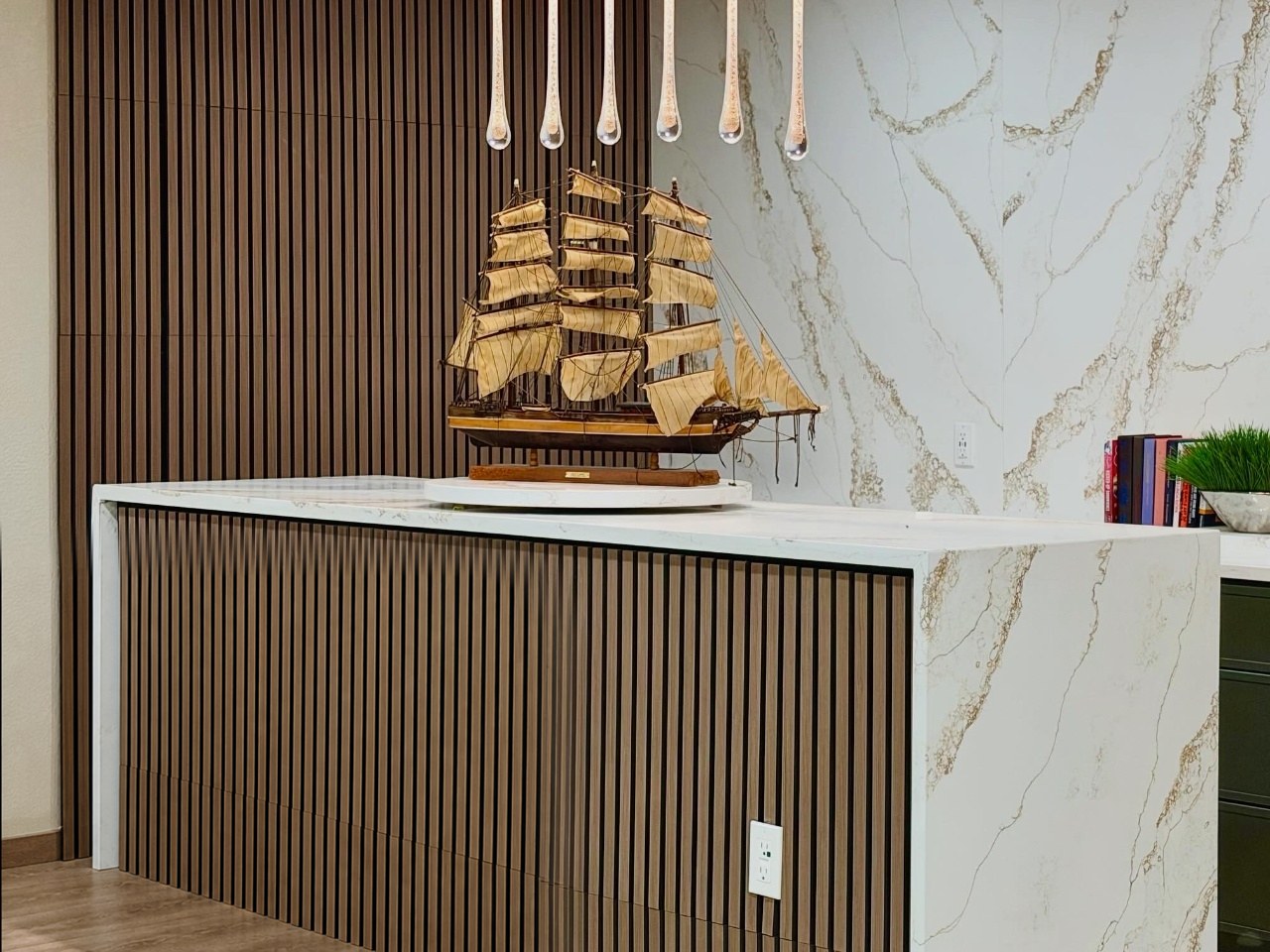 Kitchen with a waterfall quartz island, wood slat paneling and dark green drawers with brass pulls