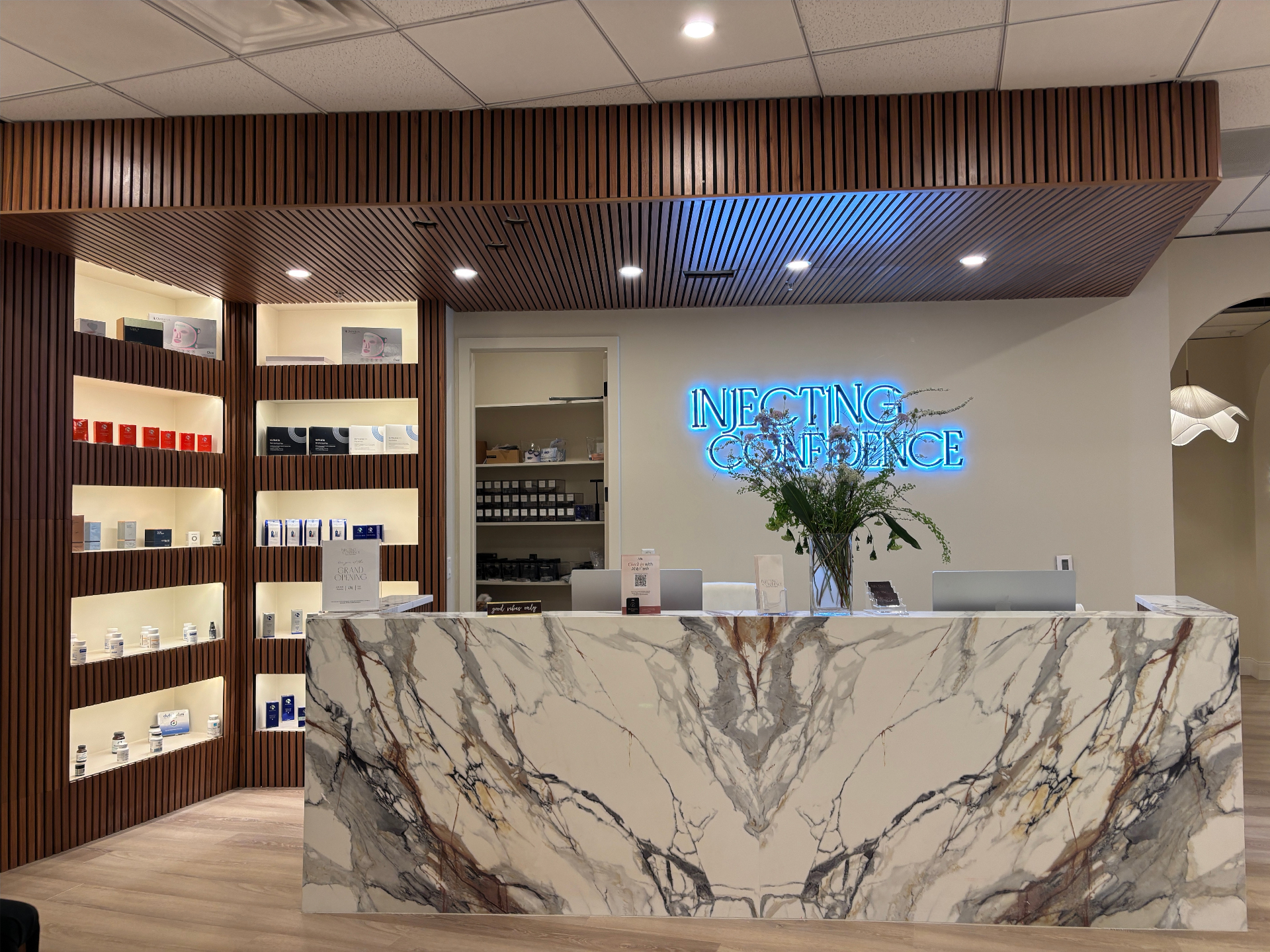 Finished reception with walnut wood slat walls and ceiling, lit niche shelves and a blue neon sign behind the marble desk
