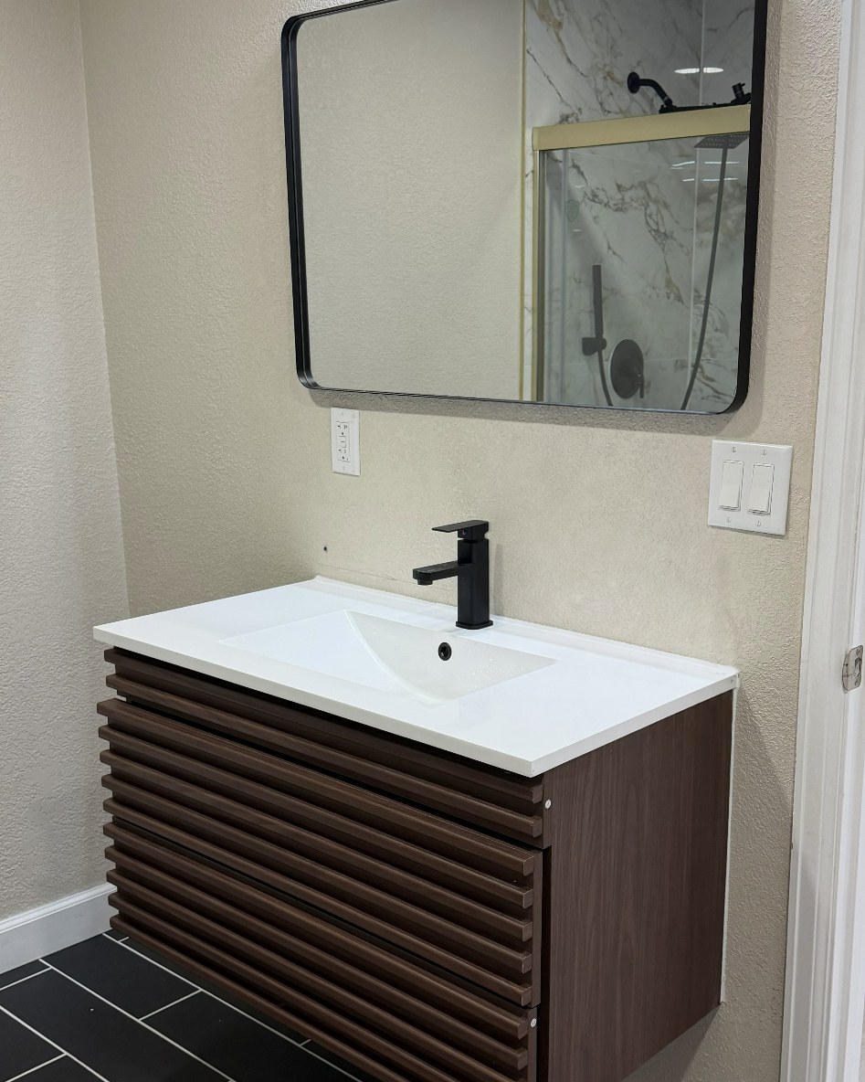Wall-mounted floating vanity in dark wood slats with a white sink top, matte black faucet and rounded black-framed mirror