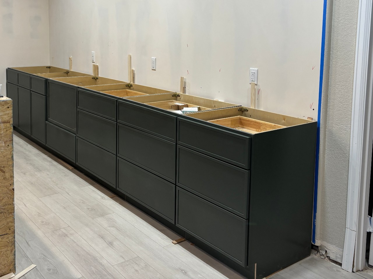 Green base cabinets set along a taped drywall wall with the unfinished island frame in place